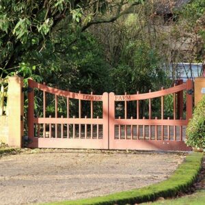 A premium Broomstick Hardwood Bespoke Gate pair featuring a sweeping curved top rail, vertical spindles, and custom engraved lettering.