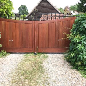 Bespoke handcrafted Utile hardwood driveway gates featuring a dipping top design and integrated black steel header, installed for a Hertfordshire property.